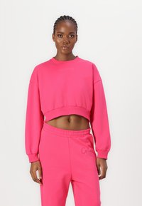 Pink cropped sweatshirt with long sleeves, ribbed cuffs, and embroidered logo at the neckline, paired with matching joggers.