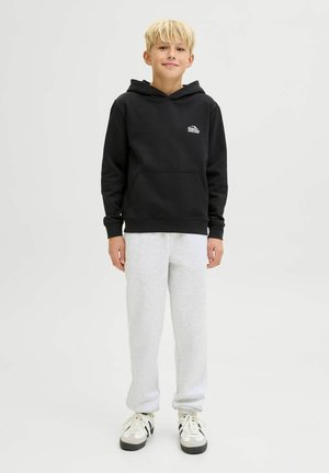 Sudadera negra con capucha, bolsillo frontal y logo, combinada con pantalones de chándal gris claro. El calzado tiene toques en blanco y negro. Ajuste casual.