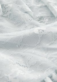 Tissu en dentelle bleu clair présentant un motif floral avec des détails élaborés et une surface délicate et texturée.