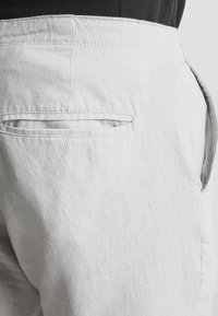 Close-up van een witte broekzak en tailleband op een persoon die een zwarte top draagt, waarbij de textuur van de stof en de stiksels duidelijk zichtbaar zijn.