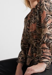 Blouse longue en voile avec un motif abstrait multicolore de feuilles aux tons terreux, dotée d'un col froncé et d'une coupe ample.
