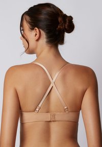 Nuder kabelloser BH mit verstellbaren, überkreuzten Trägern. Glatte Textur und minimalistisches Design, mit einem Hakenverschluss am Rücken.