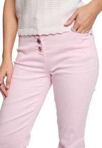Pantaloni aderenti rosa chiaro con una texture liscia, caratterizzati da tre bottoni metallici in vita e una tasca laterale.