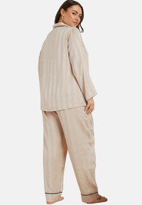 Ljusbeige randig pyjamas med mjukt tyg, som har en långärmad topp och löst sittande byxor med svarta detaljer vid muddarna.