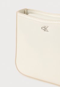 Calvin Klein krémszínű táska, varrott részletekkel, sima bőrfelülettel, enyhén lekerekített formával és egy kis ezüst logóval az oldalon.