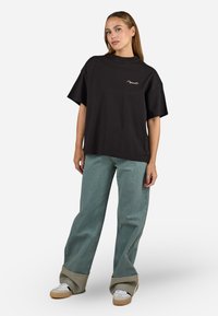 Zwarte katoenen T-shirt met hoge hals en oversized pasvorm, gecombineerd met lichtblauwe wijde jeans en beige platform sneakers.