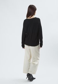 Schwarzer Langarm-Pullover mit Rundhalsausschnitt, kombiniert mit hellbeigen weiten Hosen und schwarzen High-Heels. Glatte Textur.