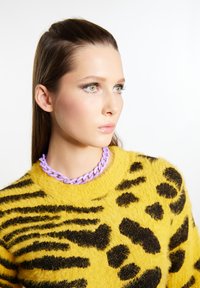 Geel sweater met zwart dierenprint, gemaakt van pluizig materiaal, gecombineerd met een chunky lavendel ketting. Close-up portretstijl.