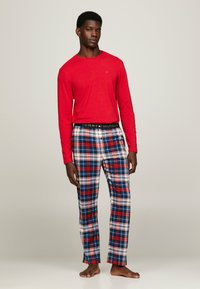 Maglietta rossa a maniche lunghe abbinata a pantaloni in flanella a quadri blu, rossi e bianchi. Presenta un elastico in vita con il logo Tommy Hilfiger.