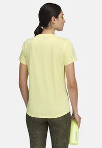 Camiseta atlética amarilla de manga corta en una tela suave y ligera con cuello redondo. Combinada con leggings texturados de color verde oscuro.