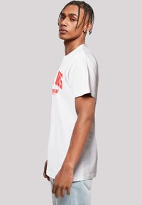 Weißes Baumwoll-T-Shirt mit rotem grafischem Text, Rundhalsausschnitt, kurzen Ärmeln und geradem Schnitt. Einfaches Design ohne zusätzliche Muster oder Akzente.