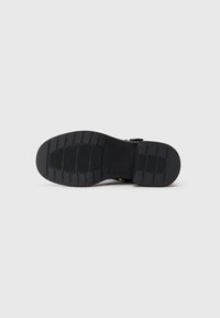 Suela de zapato negra con surcos profundos y áreas de agarre texturizadas, mostrada sobre un fondo blanco liso.