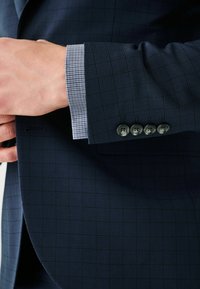 Marine geruite blazer met een gestructureerde afwerking. De manchet heeft een lichtgrijze ginghampatroon en vier donkere knopen.