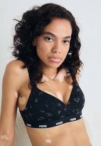 Crni bralet s teksturiranim leopard uzorkom, s v-izrezom i širokom trakom sa "PUMA" logotipom na dnu.