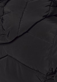 Chaqueta negra tipo puffer con una textura suave y lisa y diseño acolchado. Presenta costuras visibles y un acabado ligeramente brillante.