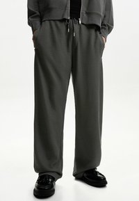 Mörkgrå sweatpants med våffelstruktur, dragsko i midjan, sidofickor och vid passform, kombinerat med svarta skor.