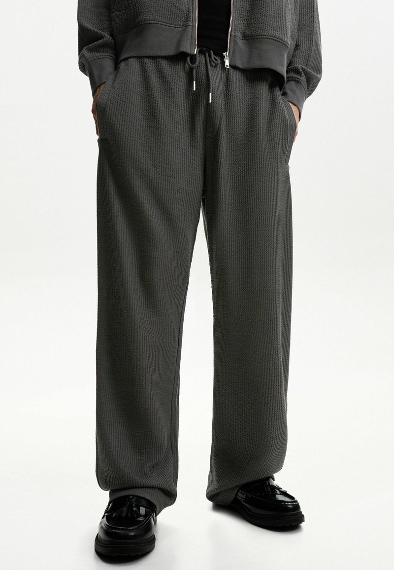 Mörkgrå sweatpants med våffelstruktur, dragsko i midjan, sidofickor och vid passform, kombinerat med svarta skor.