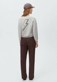 Grå kortärmad tröja med ett mörkt blixtmönster på baksidan, parat med bruna vida byxor med dekorativa nitar.