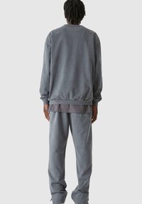 Szürke kapucnis pulóver és hozzáillő nadrág, puha anyagból készült, kényelmes szabású, bordás mandzsettákkal és réteges kialakítással. Nincsenek figyelemre méltó minták.