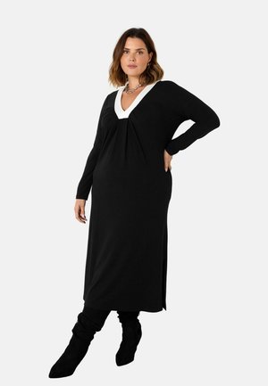 Zwarte lange mouw jurk met een V-halslijn, voorzien van witte afwerking en zijsplitten. Zacht materiaal met een ontspannen pasvorm. Bevat plooidetails.