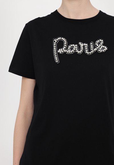 Schwarzes Baumwoll-T-Shirt mit einem mit Juwelen besetzten "Paris"-Design in Silber und weißen Perlen. Rundhalsausschnitt und kurze Ärmel. Glatte Textur.