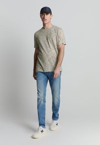 Chemise à manches courtes à rayures beige avec des rayures bleu marine, bleu et moutarde ; associée à un jean bleu clair et des baskets blanches avec des accents bleu marine.