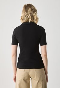 Black ribbed polo shirt with short sleeves, featuring a classic collar. Paired with beige wide-leg trousers with back pockets.