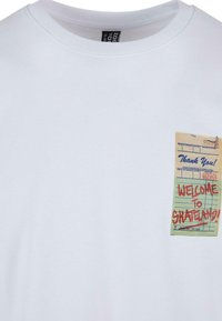 Hvid bomulds T-shirt med et lille trykt grafik af en kvitteringslignende sedel med "VELKOMMEN TIL SKATELAND!" i rødt.