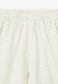 Shorts vert clair avec une taille élastique, présentant un motif de logo répété dans une teinte légèrement plus foncée. Texture de tissu lisse.