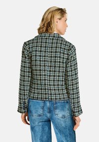 Frau, die eine schwarz-weiß-blaue karierte Jacke und blaue Jeans trägt, von hinten vor einem schlichten weißen Hintergrund gezeigt.