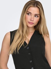 Black sleeveless dress featuring a deep V-neck, five large buttons down the front, and two side pockets. Smooth fabric texture.