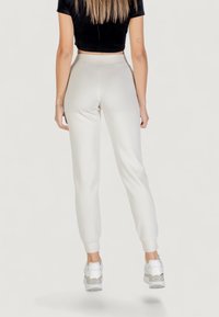 Pantaloni della tuta grigi chiari con design affusolato, dotati di polsini elastici sulle caviglie. Il materiale sembra morbido e liscio, abbinato a sneaker bianche.