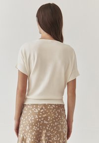 Light beige knit top with short sleeves, rounded neckline, and ribbed hem, paired with a patterned brown skirt featuring soft polka dots.