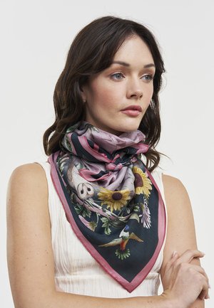 Femme aux cheveux foncés portant un haut blanc sans manches et une écharpe à motifs floraux avec des tournesols et un colibri autour du cou.