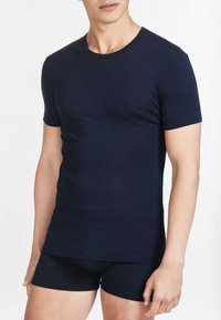 T-shirt a maniche corte color blu navy realizzato in tessuto liscio, con design aderente e collo rotondo, abbinato a pantaloni corti neri. Stile minimalista, senza fantasie.
