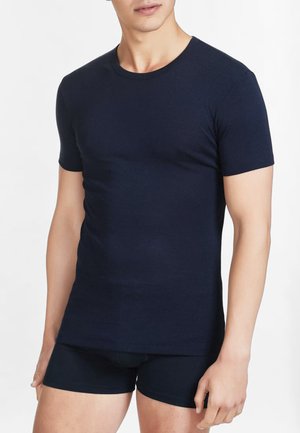 T-shirt a maniche corte color blu navy realizzato in tessuto liscio, con design aderente e collo rotondo, abbinato a pantaloni corti neri. Stile minimalista, senza fantasie.