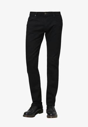 Vaqueros de denim negro con un diseño ajustado, que cuentan con cinco bolsillos, un cierre de botón frontal y detalles de costura visibles. Llevados con zapatos negros.