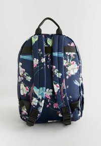 Rucsac în nuanțe marine cu flori roz și albe, păsări, bretele negre și un mâner superior. Material texturat și catarame laterale ajustabile.