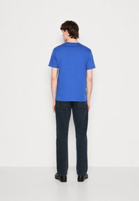 Modré bavlněné tričko s krátkým rukávem, kulatým výstřihem a hladkou texturou, doplněné tmavými džíny a černými botami.