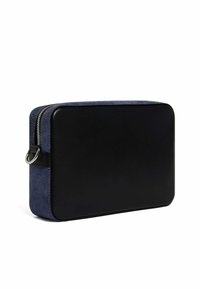 Borsa da viaggio in denim blu navy con pannello frontale nero lucido, forma rettangolare, chiusura con zip e accenti in metallo sul lato.