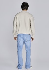 Béžová oversized mikina s kulatým výstřihem, kombinovaná se světle modrými džíny rovného střihu. Hladká textura; minimální švy na džínách.