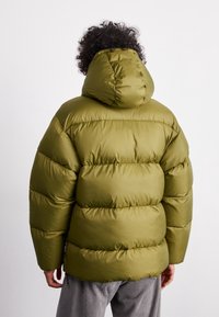 Giacca a vento verde oliva con cappuccio, caratterizzata da sezioni trapuntate e una superficie liscia e imbottita. Coulisse all'orlo per la regolabilità.