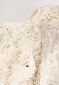 White fluffy sweater with gold sequins, alongside shiny beige fabric with round reflective spots, both featuring ribbed edges.