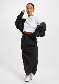 Čierna pérová bunda, biele krátke tričko a dlhá čierna sukňa. Oblečenie je doplnené bielymi teniskami. Jemná textúra látky, voľný strih.