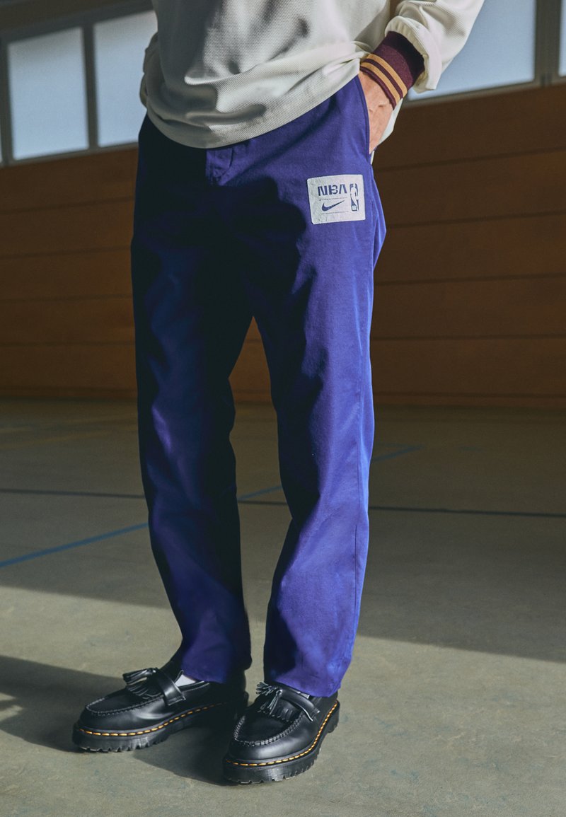 Nike NBA-merket lillastripe bukser laget av stoff, med et lappelogo, kombinert med svarte slippers med kvaster og gul søm.