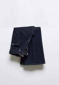 Jean en denim bleu foncé soigneusement plié, montrant la poche avant, le bouton et les détails de couture sur un fond blanc.
