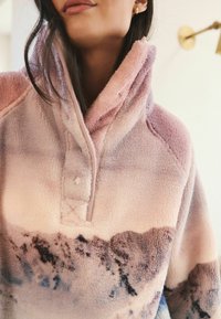 Fleece pullover with high collar; pink and purple gradient pattern; soft texture; features a partial zipper and a button closure.