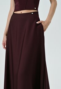 Gonna maxi bordeaux realizzata in tessuto liscio, con cinturino in vita e dettagli in metallo, oltre a una tasca laterale.