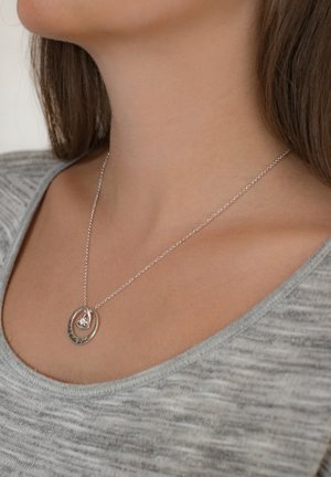 Collana con pendente in argento composto da due forme ovali interconnesse. La catena ha una finitura sottile e poggia su un top in maglia grigia. Un ovale presenta dettagli incisi.