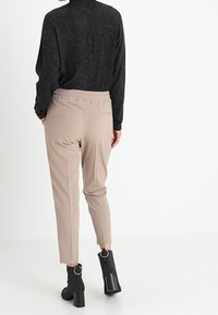 Svart långärmad topp i kombination med beige tapered-byxor. Byxorna har resårmidja och bakficka. Tillbehör inkluderar ribbade svarta ankelstövlar.